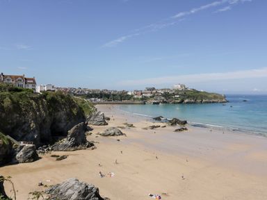 A sandy beach with rocks and cliffs by the sea and buildings on the cliffs at 33 Cliff Edge in Newquay