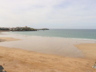 A wide beach with few people near the shoreline and a headland with buildings in the background at 33 Cliff Edge in Newquay