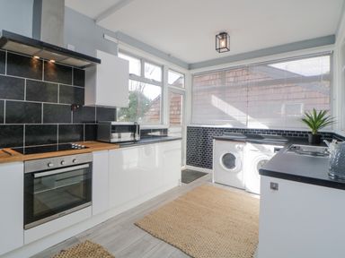 A kitchen with a built-in oven, microwave, washing machine, countertops, and rugs on the floor at Raven Cottage in Downderry