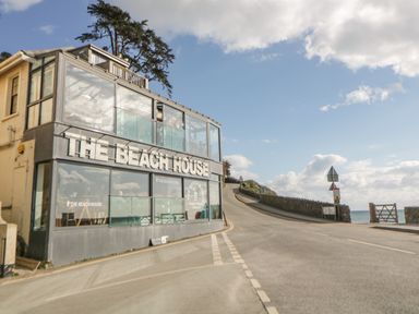 A building with large windows and a sign that says The Beach House next to a road leading to the sea