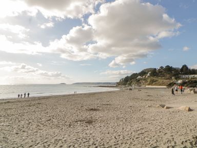 A sandy beach with people walking near the shore and houses on a hill in the background at Raven Cottage in Downderry