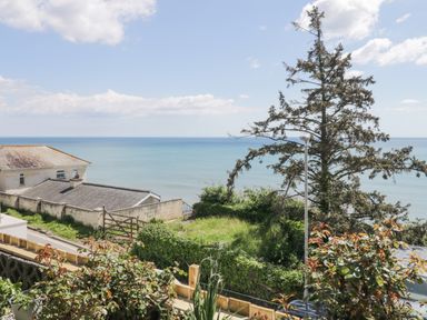 View of the sea with houses trees a street and plants in a garden at Raven Cottage in Downderry