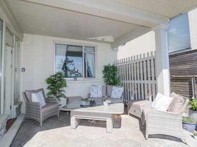 A covered patio with wicker chairs sofa a glass table and potted plants at Raven Cottage in Downderry