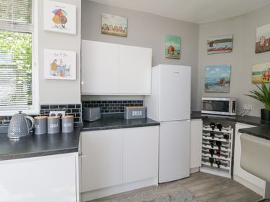 A kitchen with white cabinets black countertops a white refrigerator a microwave and a wine rack at Raven Cottage in Downderry