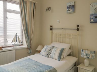 A bedroom with a bed with pillows and a quilt beside a window with striped curtains at Raven Cottage in Downderry