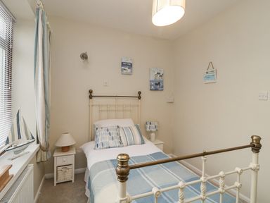 A small bedroom with a single bed two bedside tables lamps and a window with curtains at Raven Cottage in Downderry