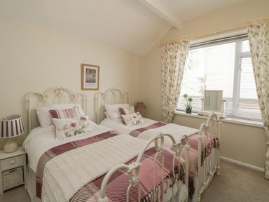 A bedroom with two single beds bedside table and window with floral curtains at Raven Cottage in Downderry