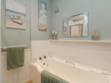 A bathroom with a bathtub towels a mirror and beach themed decor at Raven Cottage in Downderry