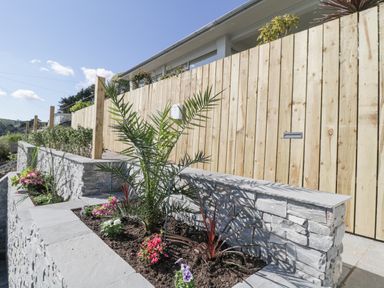 A garden with stone planters and various plants next to a wooden fence at Raven Cottage in Downderry