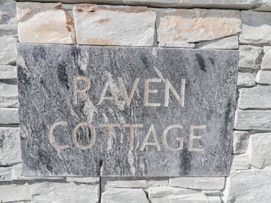 A stone wall with a grey marble plaque engraved with the words Raven Cottage at Raven Cottage in Downderry