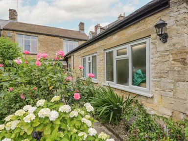 A garden with pink and white flowers next to a stone house with white windows and an outdoor lamp at 2 Church Street in Chipping Norton