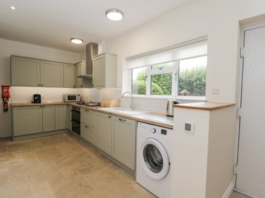 A kitchen with cabinets a washing machine a microwave and a window at 2 Church Street in Chipping Norton
