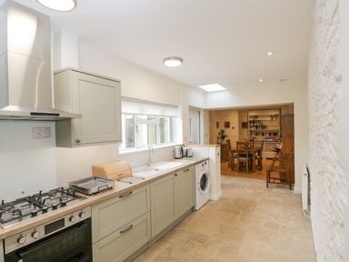 A kitchen with stove, sink, washing machine, and dining area with wooden table and chairs at 2 Church Street in Chipping Norton