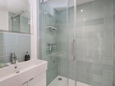 A bathroom with a white sink and a glass-enclosed shower area with light green tiled walls at 2 Church Street in Chipping Norton
