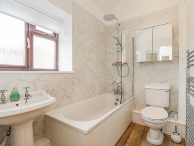 A bathroom with a bathtub shower combo toilet pedestal sink and towel radiator at 2 Church Street in Chipping Norton