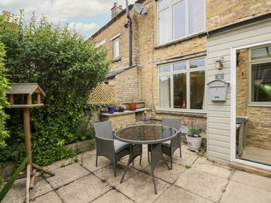 A small outdoor patio with a round table and three chairs next to a stone house at 2 Church Street in Chipping Norton
