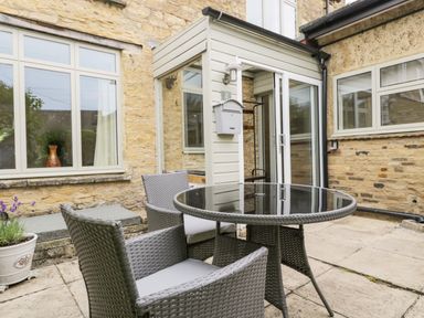 An outdoor patio area with a round glass table and four grey wicker chairs outside a stone building at 2 Church Street in Chipping Norton