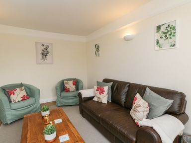 A living room with a brown leather sofa two green armchairs a wooden coffee table and wall art at 2 Church Street in Chipping Norton