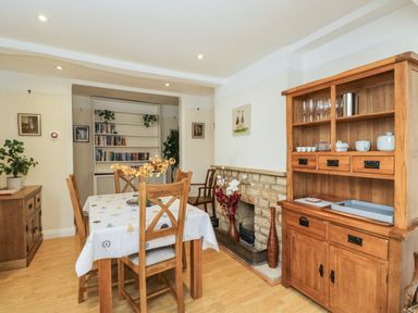A dining room with a wooden table and chairs a sideboard a bookshelf and a stone fireplace at 2 Church Street in Chipping Norton