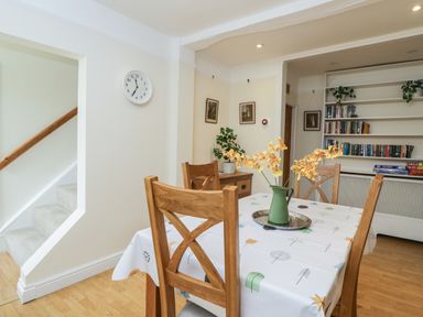 A dining area with a table covered by a tablecloth and wooden chairs next to a staircase and bookshelf at 2 Church Street in Chipping Norton