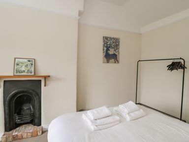 A bedroom with a bed with folded towels a black metal clothes rack and a small fireplace at 2 Church Street in Chipping Norton