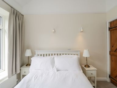 A bedroom with a white bed and pillows two bedside tables with lamps and beige curtains at 2 Church Street in Chipping Norton