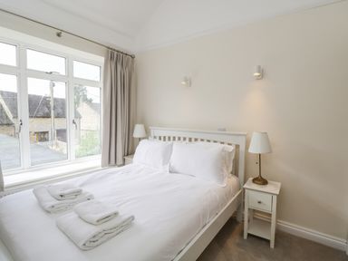 A bedroom with a double bed white bedding bedside tables lamps and a large window at 2 Church Street in Chipping Norton