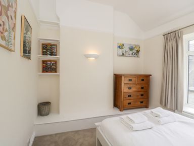 A bedroom with a wooden chest of drawers a bed with white linens and towels and framed pictures on the walls at 2 Church Street in Chipping Norton