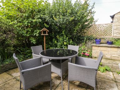 A patio with a round table and four chairs surrounded by plants and a stone wall at 2 Church Street in Chipping Norton