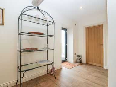 A hallway with a metal shelf holding plates and mugs next to a glass door and wooden door at Palace Farmhouse in St Weonards