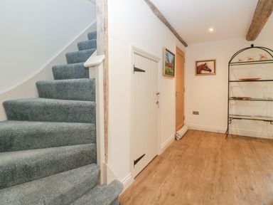 A hallway with carpeted stairs small door paintings on walls and a metal shelving unit at Palace Farmhouse in St Weonards