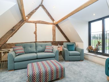 A sitting area with a blue sofa, blue armchair, patterned ottoman, side tables, and a window with a view at Palace Farmhouse in St Weonards