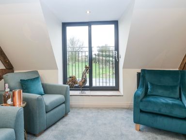 A sitting area with two armchairs a metal rooster figure on the window sill and a bottle on a small side table at Palace Farmhouse in St Weonards