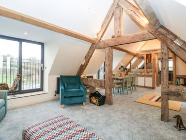 A living room with a teal armchair a patterned ottoman wooden beams a dining table with chairs and large windows at Palace Farmhouse in St Weonards