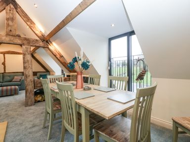 A dining area with a wooden table and chairs near a large window and exposed wooden beams at Palace Farmhouse in St Weonards