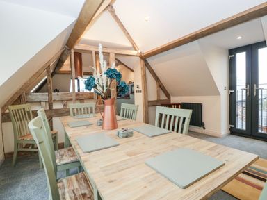 A dining area with a wooden table and six chairs with placemats and a vase with flowers at Palace Farmhouse in St Weonards