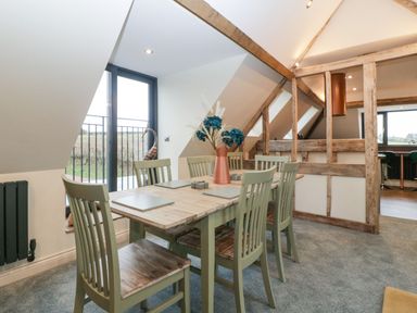 A dining area with a wooden table surrounded by six chairs and a vase with flowers on the table at Palace Farmhouse in St Weonards