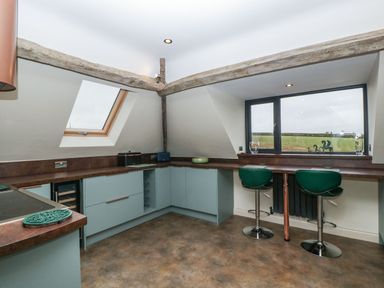 A kitchen with blue cabinets wooden countertops two green bar stools and exposed wooden beams at Palace Farmhouse in St Weonards