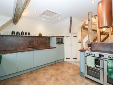 A kitchen with blue cabinets wooden beams and a stainless steel oven at Palace Farmhouse in St Weonards