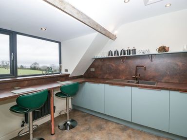A kitchen with green stools under a counter and a sink with cabinets and a shelf above at Palace Farmhouse in St Weonards