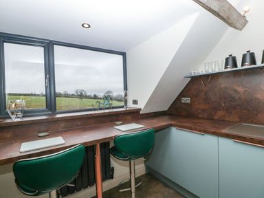 A kitchen area with two green bar stools under a brown countertop and a window overlooking a field at Palace Farmhouse in St Weonards
