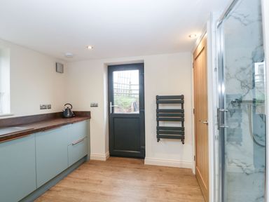 A utility room with blue cabinets a black door a wooden floor a wall-mounted black radiator and a shower at Palace Farmhouse in St Weonards