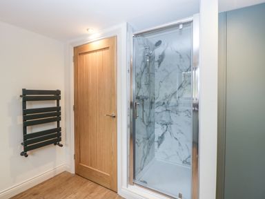 A bathroom with a wooden door a black towel radiator and a glass shower enclosure with marble patterned walls at Palace Farmhouse St Weonards