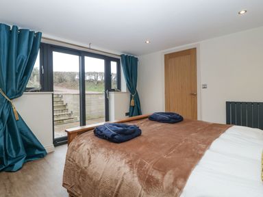 A bedroom with a brown blanket on the bed blue towels on top blue curtains and glass doors leading outside at Palace Farmhouse in St Weonards