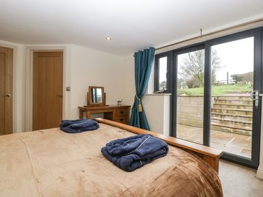 A bedroom with a bed and folded robes on it near windows with blue curtains and wooden furniture at Palace Farmhouse in St Weonards