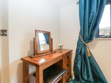 A wooden dressing table with a mirror and small flower vase next to a window with blue curtains at Palace Farmhouse in St Weonards