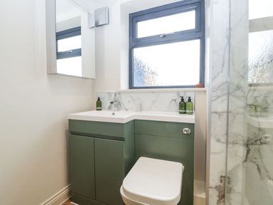A bathroom with a green vanity unit with a sink and a toilet under a window at Palace Farmhouse in St Weonards