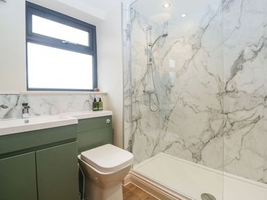 A bathroom with a green vanity unit with sink a white toilet and a shower with marble walls at Palace Farmhouse in St Weonards