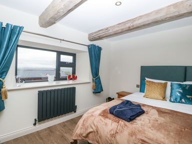 A bedroom with a bed with pillows and a folded robe on a blanket next to a window with blue curtains and wooden beams on the ceiling at Palace Farmhouse in St Weonards