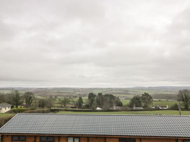 A landscape view with fields trees and houses behind a building with a tiled roof at Palace Farmhouse in St Weonards